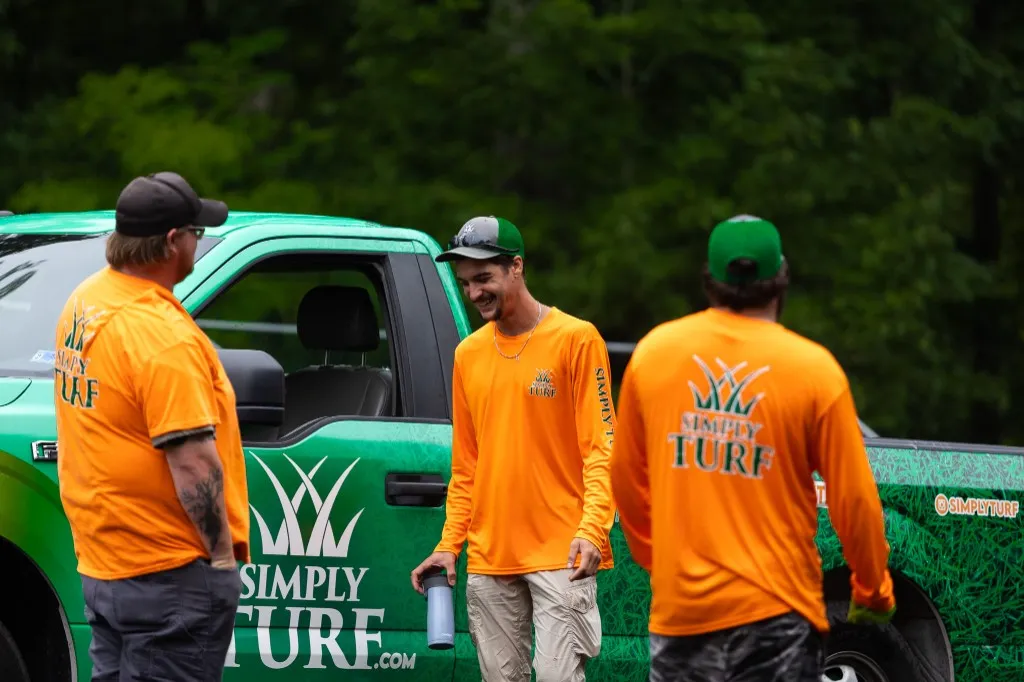 Three Simply Turf technicians in orange shirts beside a green Simply Turf truck