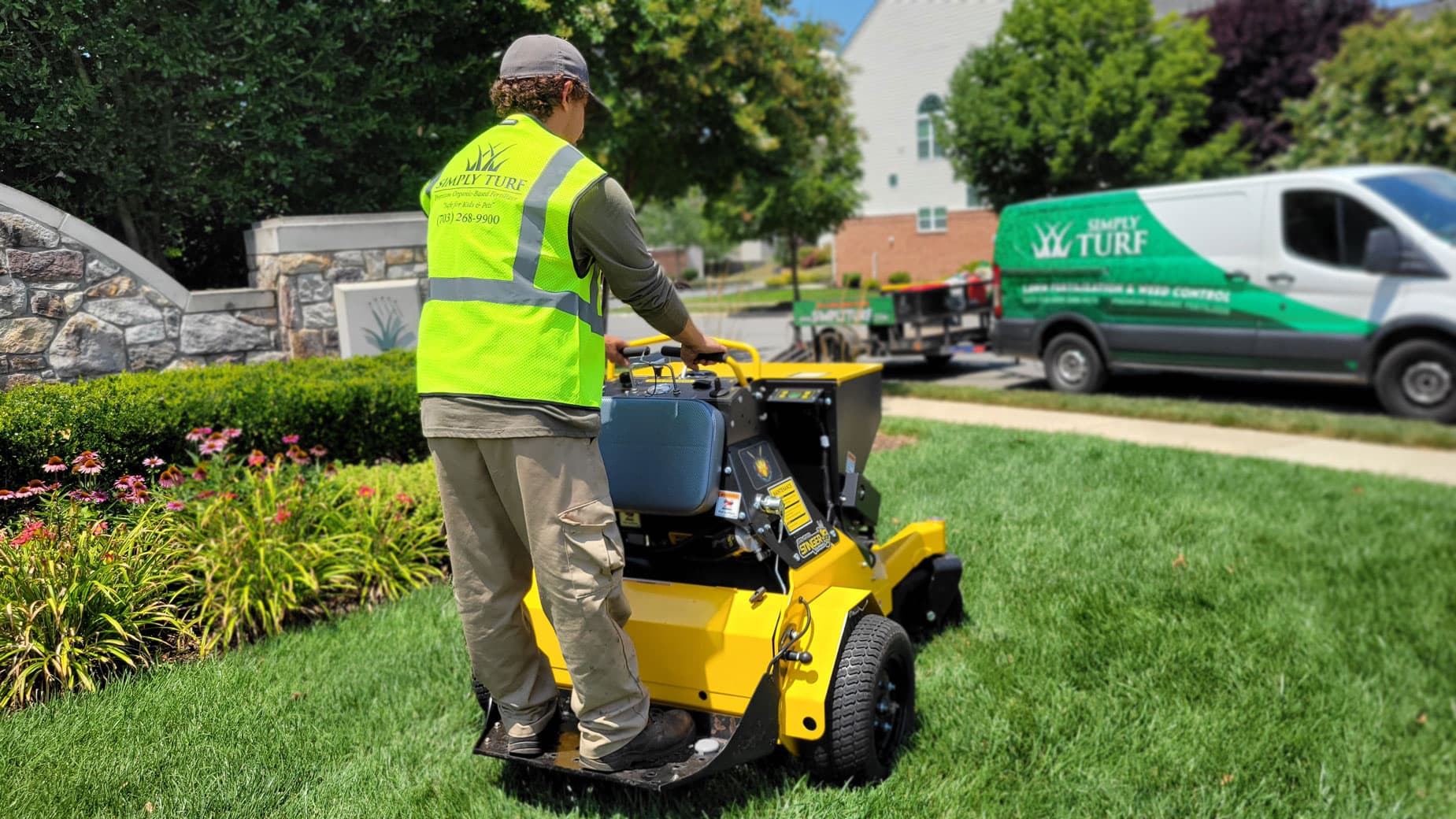 Simply Turf technician operating a stand-on Stinger aerator with seed box